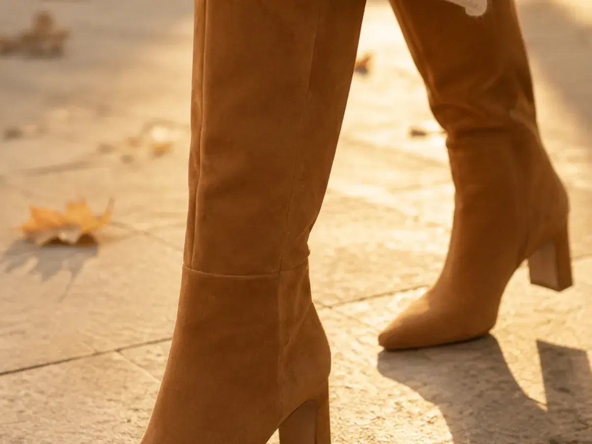 Cognac suede knee-high boots mid-stride on pale stone in low autumn sun
