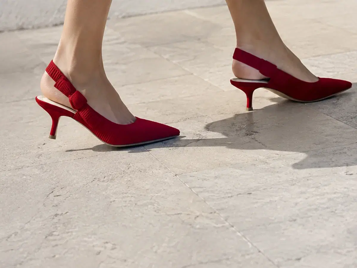 Red ribbed-knit slingback kitten heels mid-stride on pale limestone