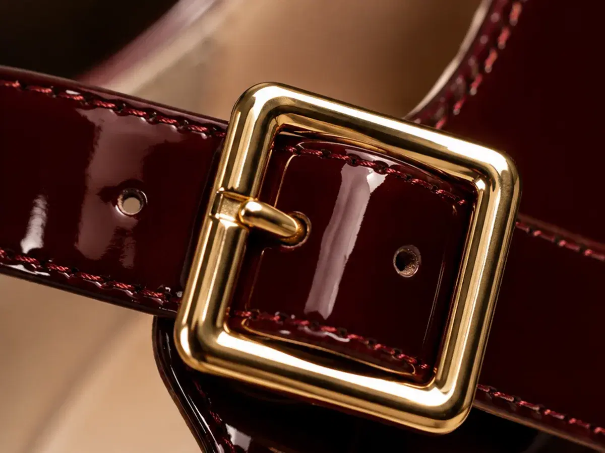 Macro of the square gold buckle, patent strap stitching and cream lining