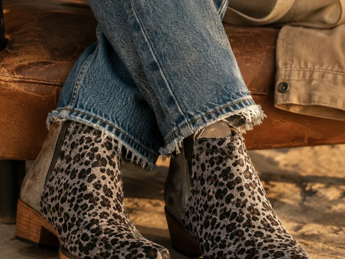 Seated on a leather bench, boots with cropped denim in warm afternoon light